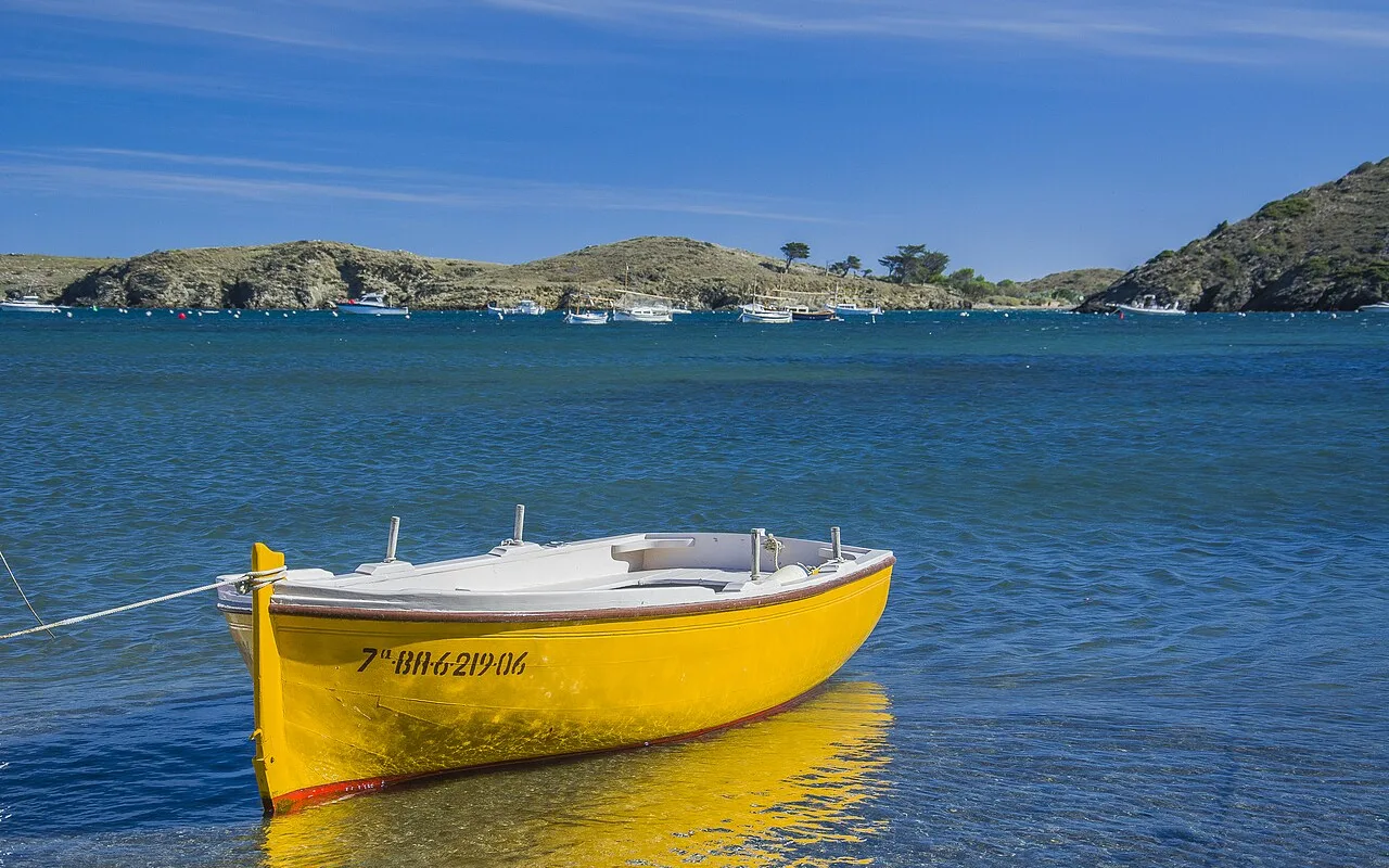 A yellow wooden fishing boat moored in the clear water of Portlligat cove
