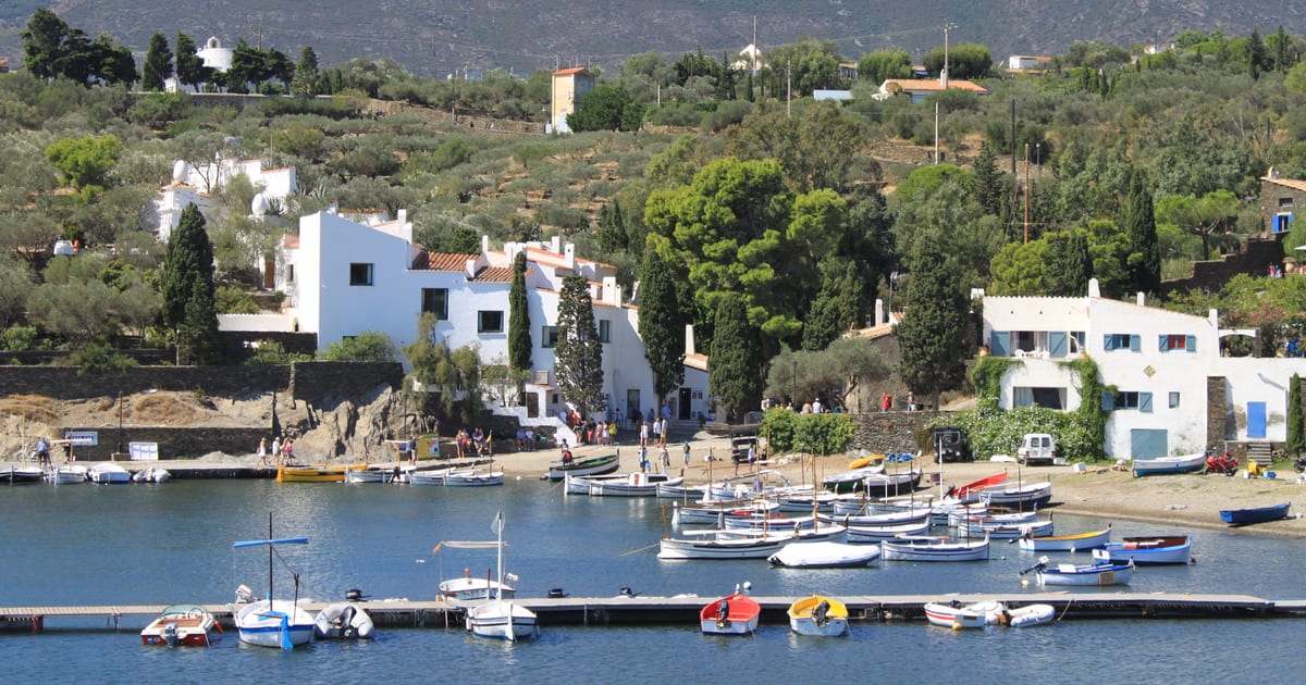 Whitewashed house of Salvador Dalí above Portlligat cove, with fishing boats moored in front and the Cap de Creus hills behind